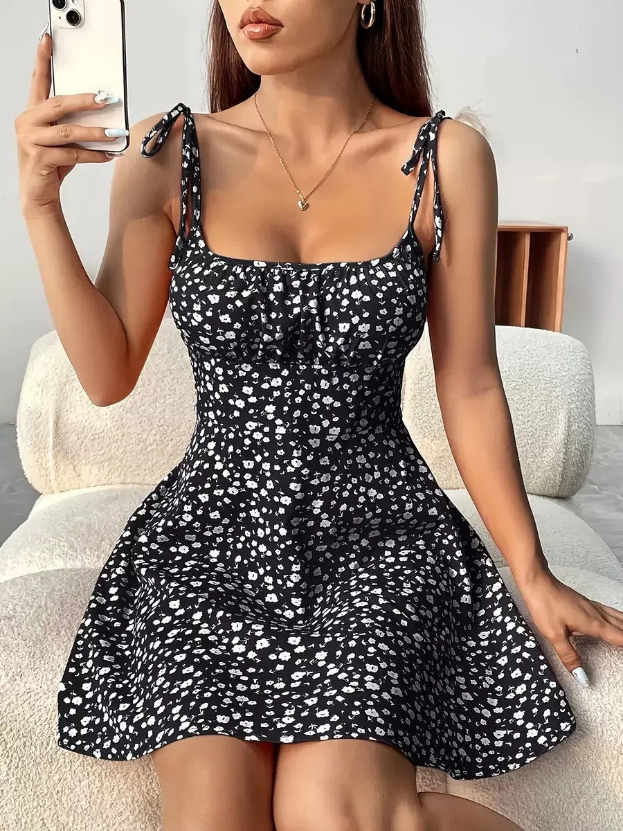 Woman wearing a black floral dress sitting on a white couch.
