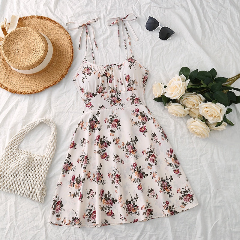 Floral dress with straw hat, bag, and flowers on a light background