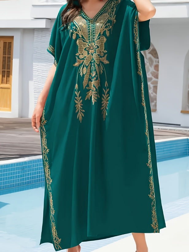A woman wearing a flowing teal green kaftan dress with ornate gold embroidery around the V-neck and along the side seams, standing by a swimming pool.