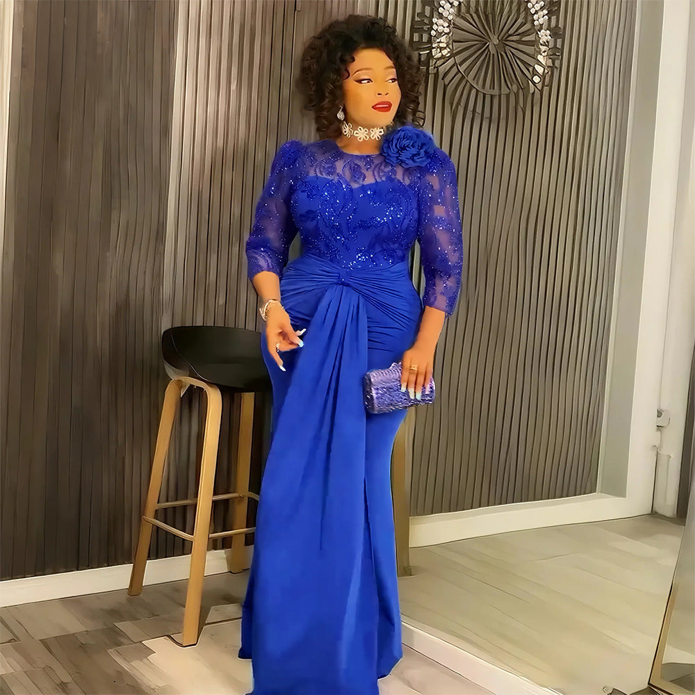 A woman wearing a royal blue lace and satin evening gown with a ruched waist, holding a matching blue clutch in front of a modern slatted wood wall.