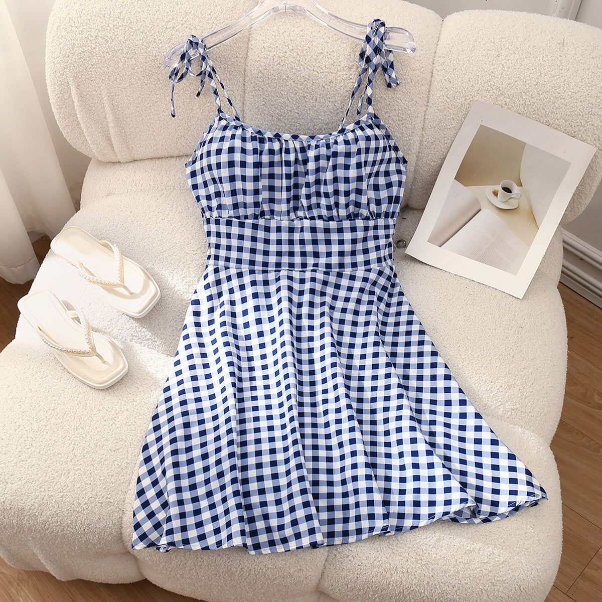 Blue and white checkered dress on a hanger against a beige sofa.