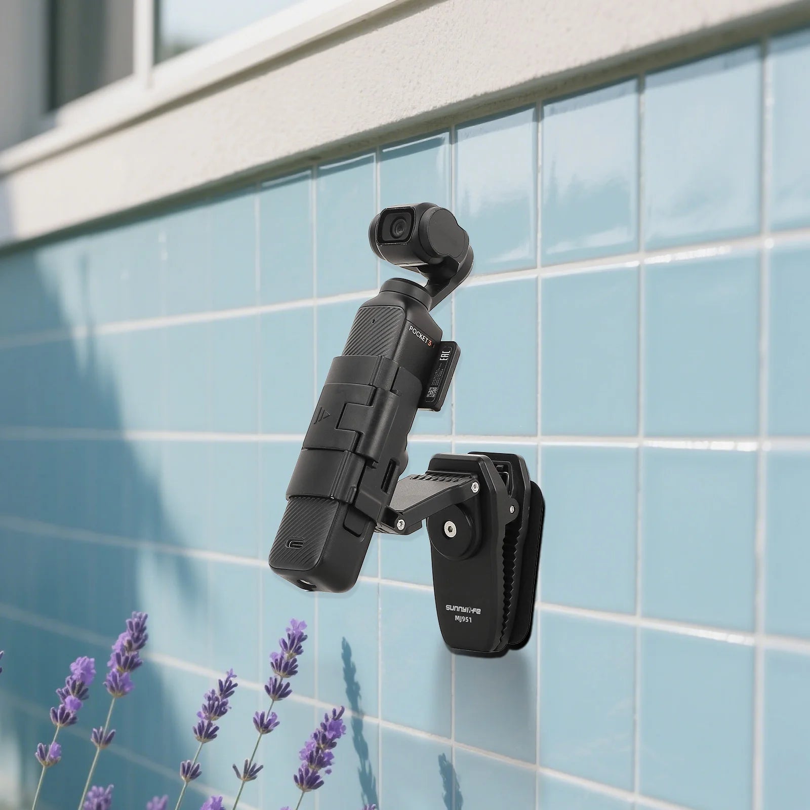 A black SUNNYLIFE backpack clip mount attached to a backpack strap, securing a DJI Pocket 3 camera stabilizer against a blue tiled wall.