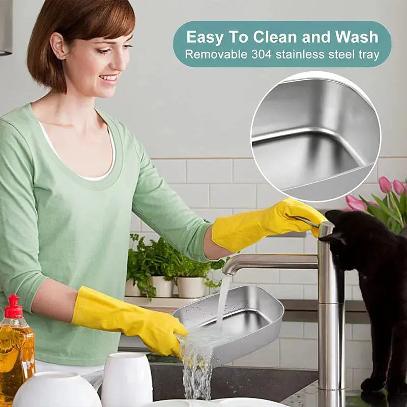 An infographic showing a woman in a kitchen wearing yellow rubber gloves while washing the removable 304 stainless steel inner tray under running tap water next to a black cat, featuring a circular inset close-up of the clean tray corner.