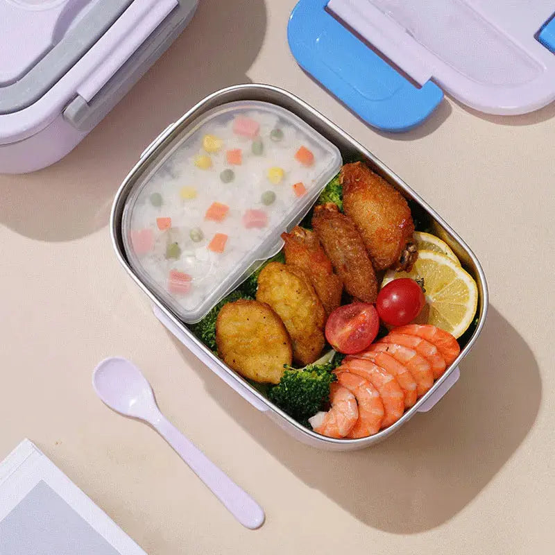 A top-down view of the 1.5L removable food-grade stainless steel inner tray inside the light purple electric lunch box, filled with chicken wings, fried shrimp, broccoli, tomatoes, lemons, and a separate sealed container of mixed rice, next to a matching plastic spoon.