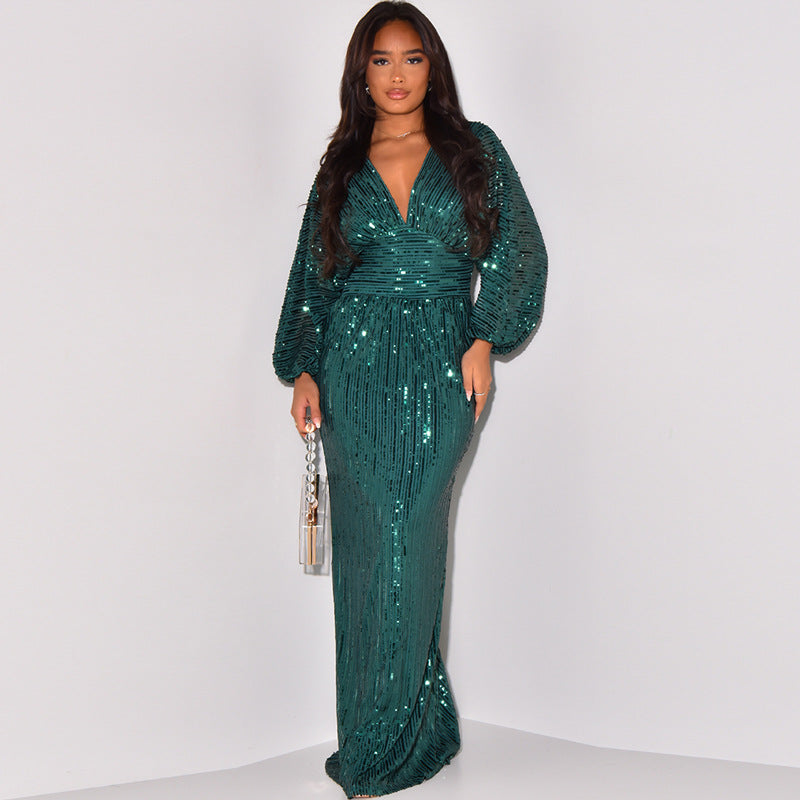 A woman modeling a floor-length, deep V-neck gown covered in shimmering teal sequins, featuring balloon sleeves and a fitted waist, standing against a plain light gray studio background.