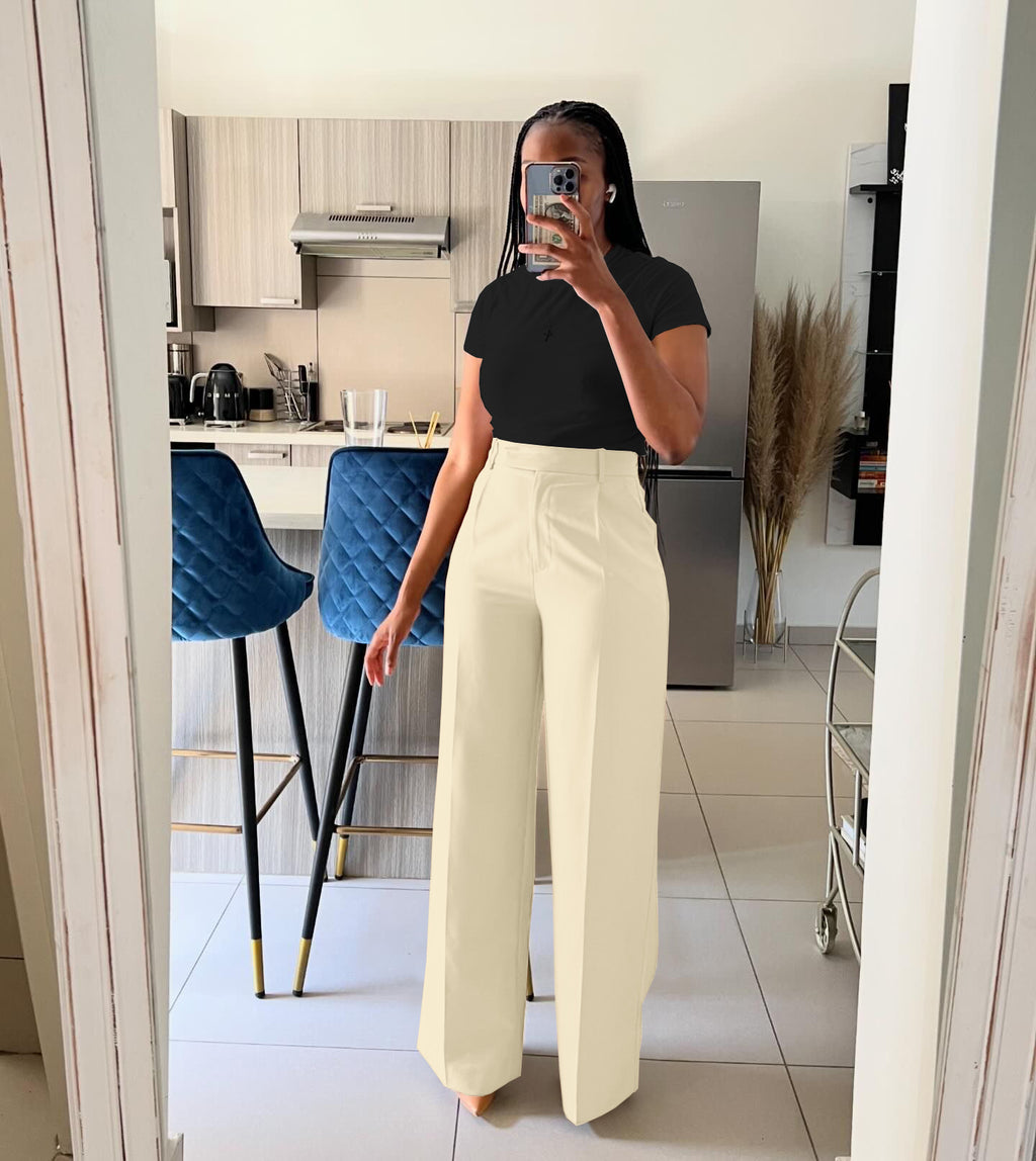 Person taking a mirror selfie wearing a black top and white pants in a kitchen.