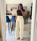 Person taking a mirror selfie wearing a black top and white pants in a kitchen.