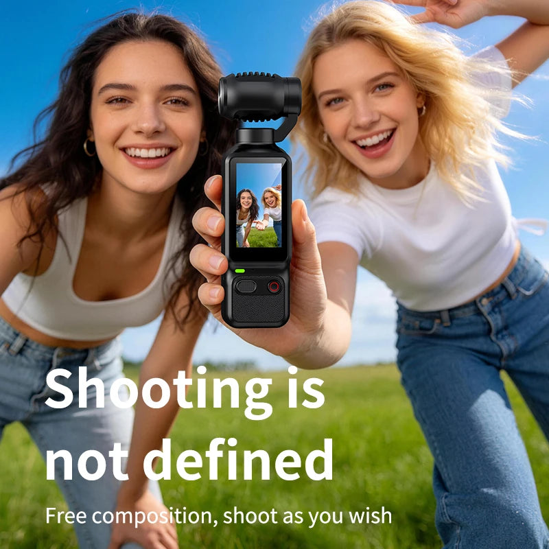 Two cheerful young women taking an outdoor selfie using a compact handheld gimbal camera with a live preview screen, surrounded by a green grassy field and blue sky.