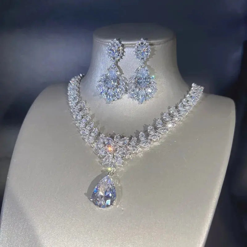 A luxurious moissanite pendant necklace and matching earring set displayed on a mannequin bust against a soft-focus background.